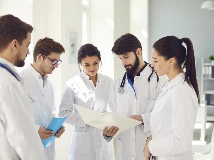 A group of students wearing lab coats gather 和 observe health chart in hospital setting